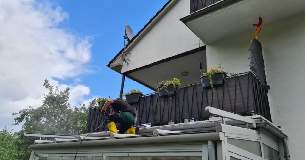 Un homme accroupi nettoie le toit d'une véranda attenante à une maison. 
